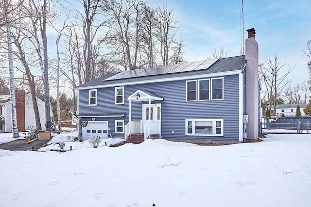 split foyer home featuring an attached garage, a chimney, and solar panels