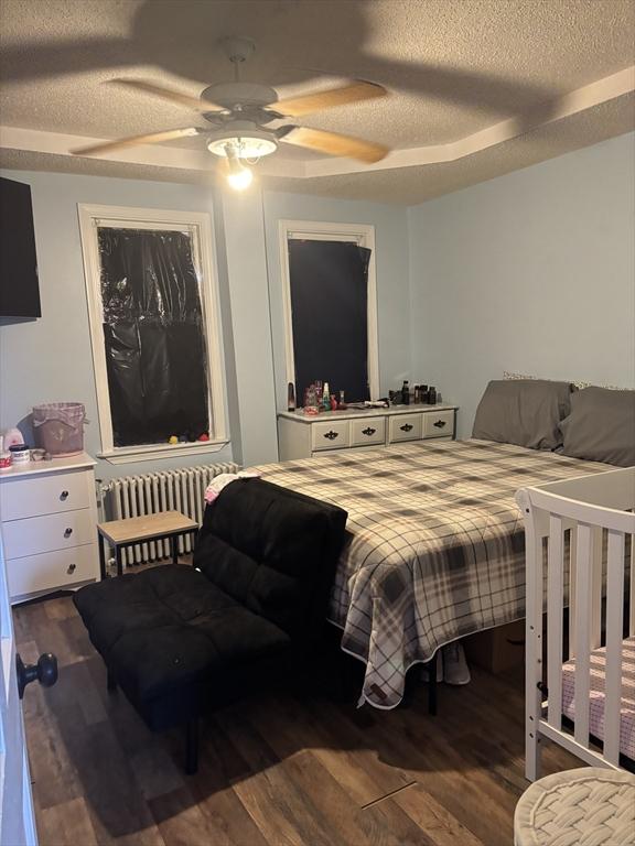 bedroom featuring dark wood-type flooring, ceiling fan, a textured ceiling, and radiator heating unit