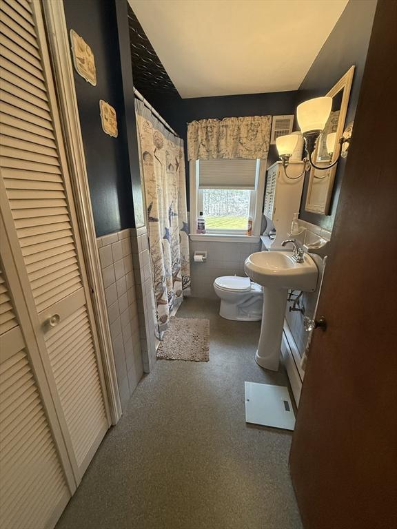 bathroom with a sink, wainscoting, curtained shower, tile walls, and toilet