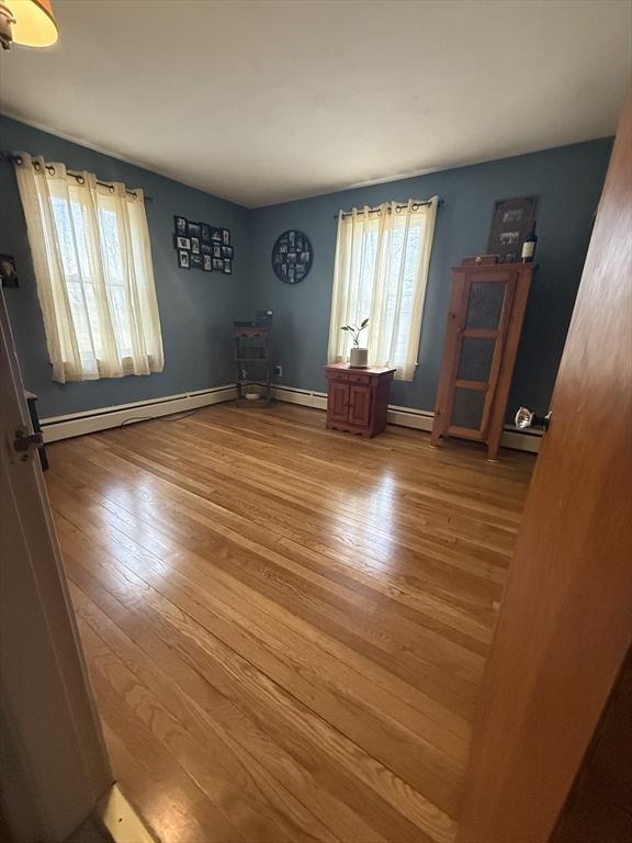 interior space featuring a baseboard heating unit, baseboards, and wood finished floors