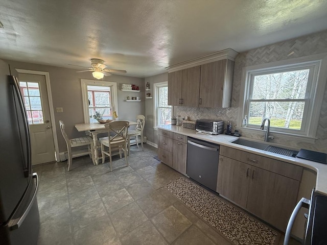 kitchen with a sink, tasteful backsplash, stainless steel dishwasher, freestanding refrigerator, and light countertops