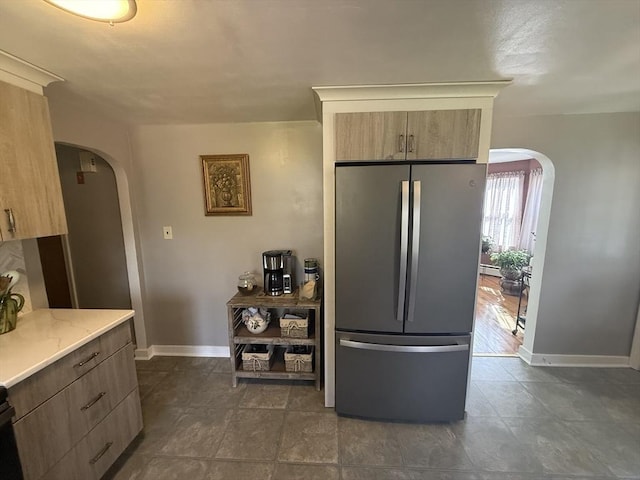 kitchen featuring light stone counters, arched walkways, freestanding refrigerator, and a baseboard radiator