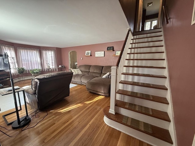 living area with arched walkways, stairway, a baseboard radiator, and wood finished floors