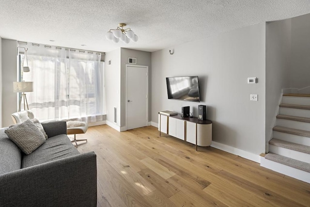 living room with baseboards, a textured ceiling, stairs, and light wood finished floors