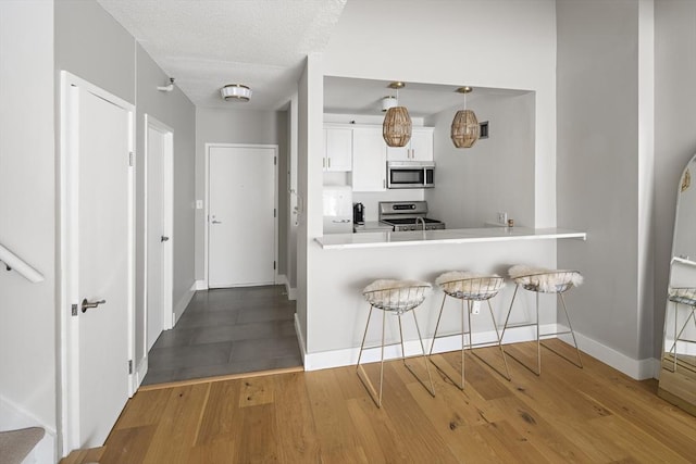 kitchen featuring baseboards, a kitchen breakfast bar, wood finished floors, and stainless steel appliances
