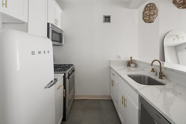 kitchen featuring light stone counters, a sink, stainless steel appliances, white cabinetry, and visible vents