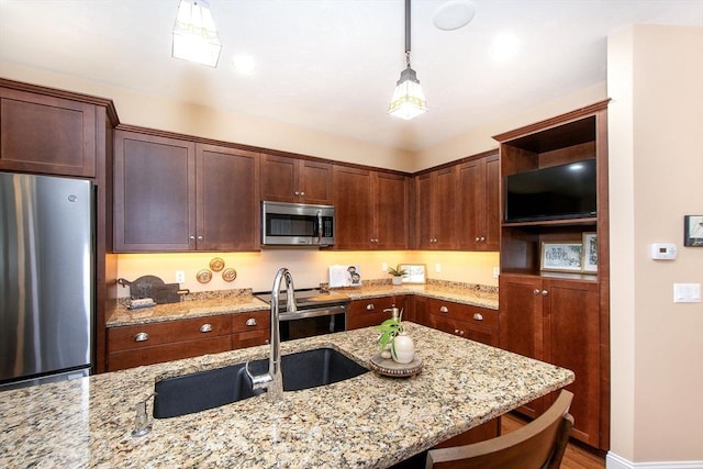 kitchen with stainless steel appliances, a sink, light stone countertops, a kitchen bar, and decorative light fixtures