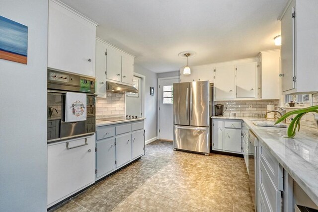 kitchen with stainless steel appliances, under cabinet range hood, a sink, tasteful backsplash, and light countertops