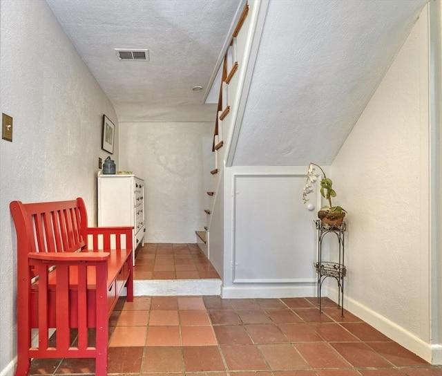 corridor with a textured wall, stairs, tile patterned flooring, and a textured ceiling