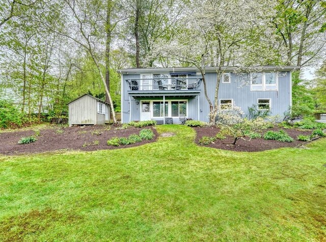 back of house with a storage shed, an outdoor structure, a yard, and a balcony