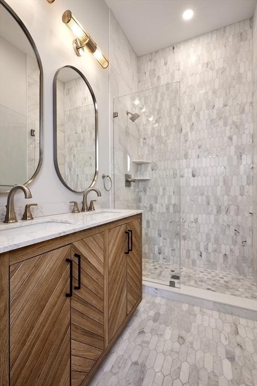 full bathroom with tiled shower, double vanity, and a sink