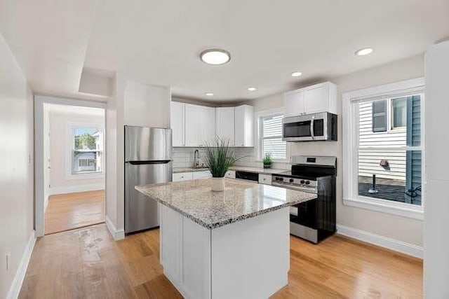 9 Foster St Unit 2, Gloucester, MA 01930 - kitchen with stainless steel appliances, light stone countertops, white cabinets, light wood-style flooring, and a kitchen island