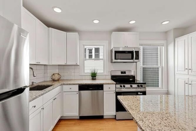 9 Foster St Unit 2, Gloucester, MA 01930 - kitchen with stainless steel appliances, white cabinets, light wood-style floors, recessed lighting, and light stone countertops