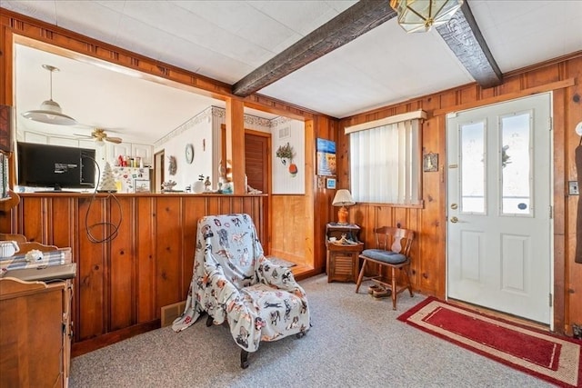 sitting room featuring light carpet, beam ceiling, ceiling fan, and wood walls