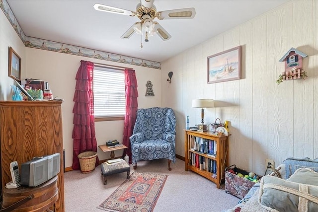 sitting room with wood walls, carpet floors, and ceiling fan