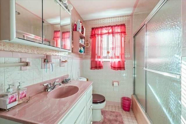 full bathroom with vanity, toilet, combined bath / shower with glass door, and tile walls