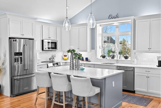 kitchen featuring a breakfast bar area, a sink, light wood-style floors, vaulted ceiling, and appliances with stainless steel finishes