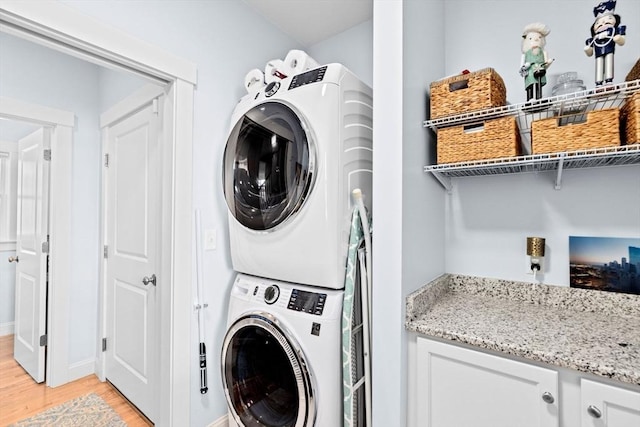 washroom featuring stacked washer and dryer, laundry area, light wood-style floors, and baseboards