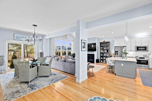 dining room with light wood finished floors, recessed lighting, a glass covered fireplace, and an inviting chandelier