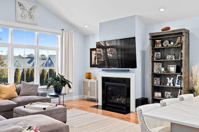 living area featuring baseboards, lofted ceiling, a fireplace with flush hearth, light wood-type flooring, and recessed lighting