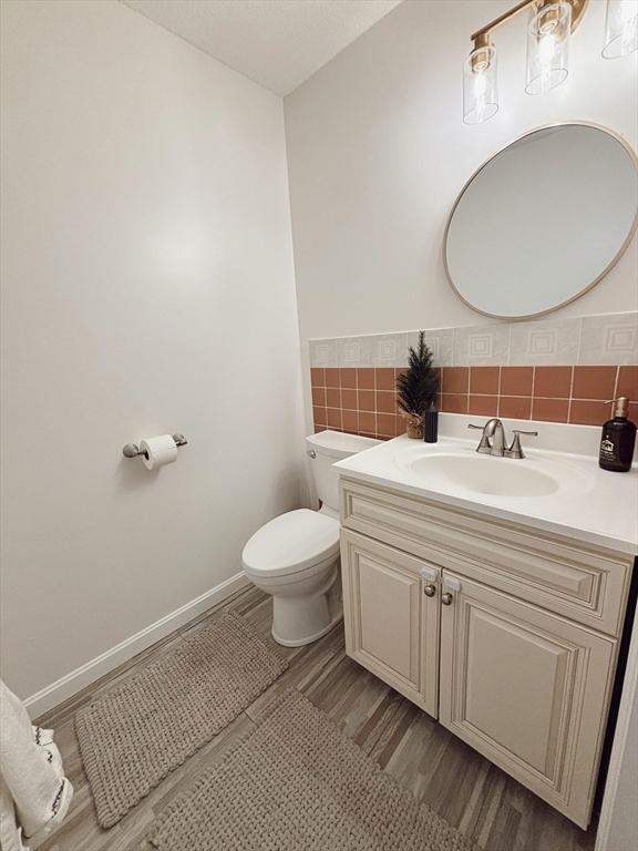 bathroom with backsplash, hardwood / wood-style floors, toilet, vanity, and tile walls