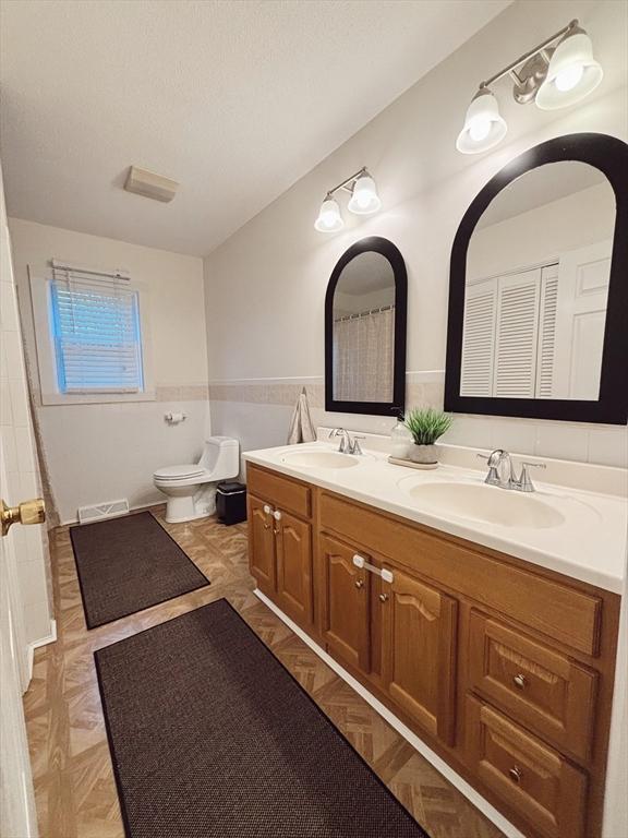 bathroom with parquet floors, vanity, toilet, and tile walls