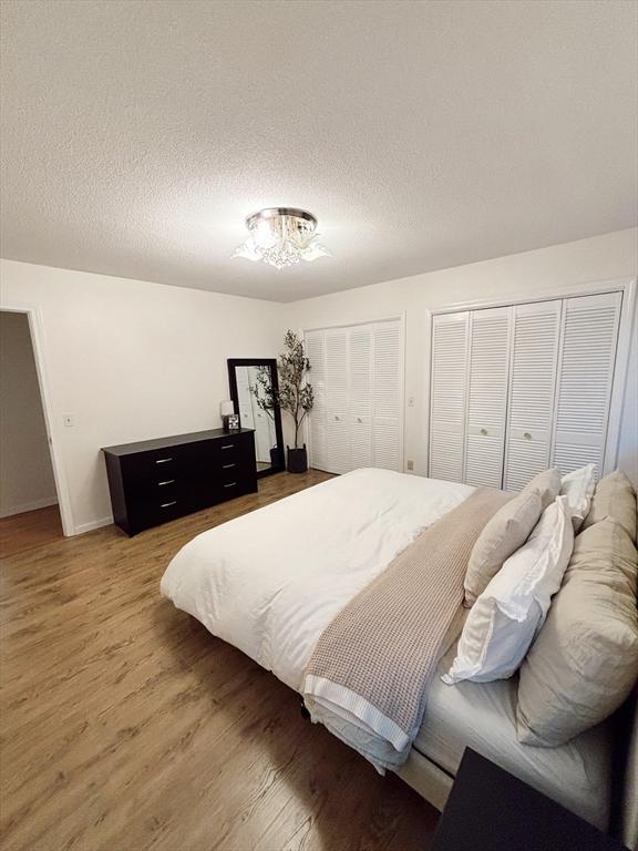 bedroom featuring hardwood / wood-style flooring, a textured ceiling, and multiple closets