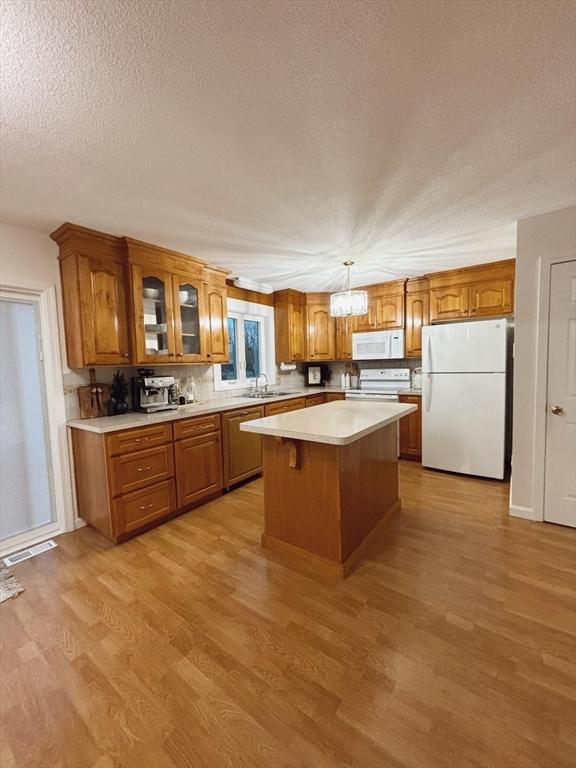 kitchen with a center island, white appliances, hanging light fixtures, light wood-type flooring, and a textured ceiling