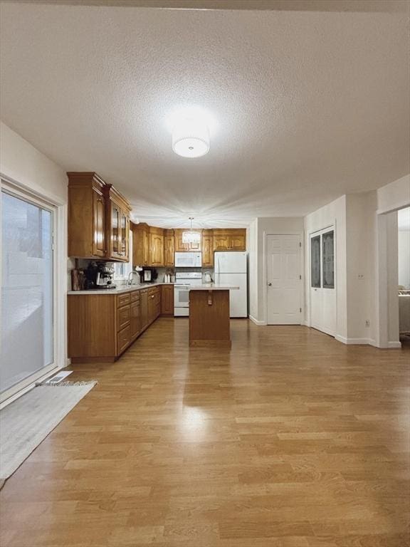 kitchen with a textured ceiling, white appliances, and light hardwood / wood-style flooring