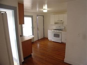 kitchen featuring white cabinets, dark hardwood / wood-style flooring, white range with gas stovetop, and radiator heating unit