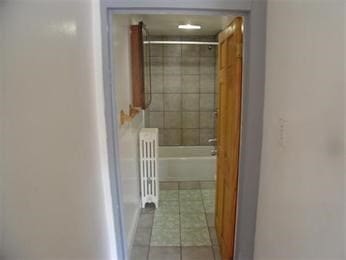 bathroom featuring tile patterned floors, radiator, and a tile shower