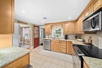 kitchen featuring sink, light stone counters, decorative backsplash, light tile patterned floors, and appliances with stainless steel finishes