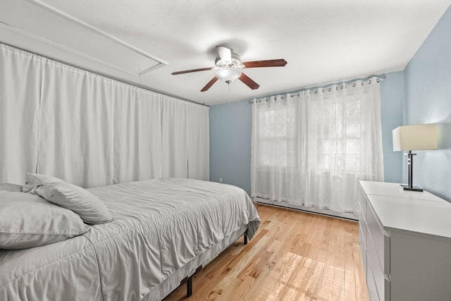 bedroom featuring light wood-type flooring, ceiling fan, and a baseboard heating unit