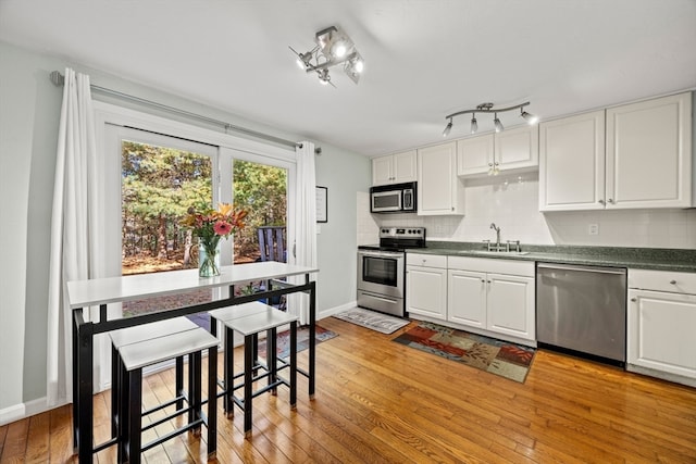 kitchen with stainless steel appliances, light hardwood / wood-style floors, sink, backsplash, and white cabinetry