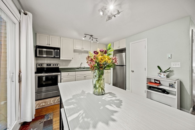 kitchen with tasteful backsplash, stainless steel appliances, white cabinetry, sink, and hardwood / wood-style floors