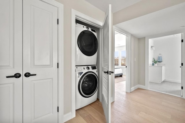 laundry area with laundry area, light wood-style flooring, stacked washer and clothes dryer, and baseboards