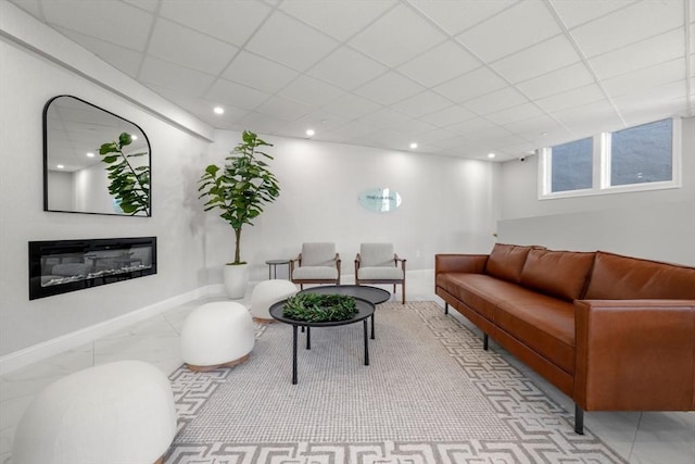 living room with a glass covered fireplace, recessed lighting, a paneled ceiling, and baseboards