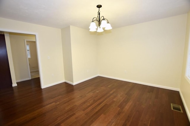 empty room featuring dark wood-type flooring and an inviting chandelier