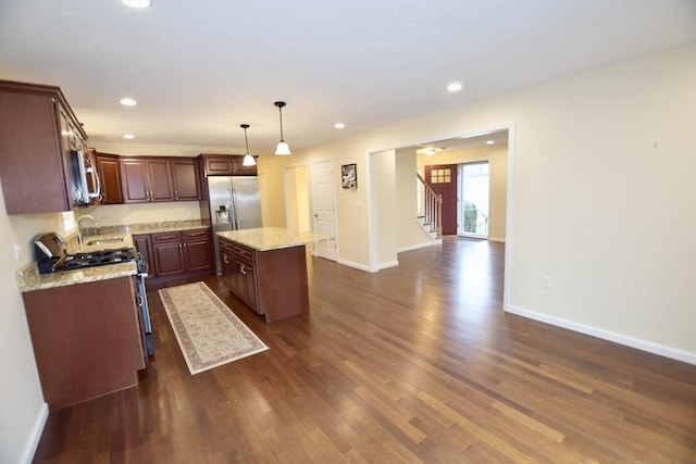 kitchen featuring hanging light fixtures, dark hardwood / wood-style floors, light stone countertops, appliances with stainless steel finishes, and a kitchen island