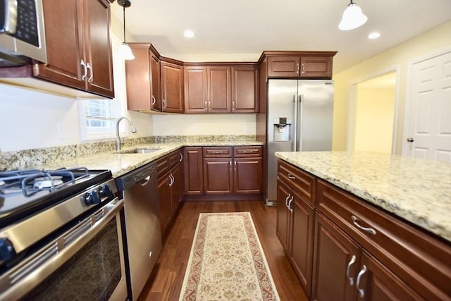 kitchen featuring appliances with stainless steel finishes, light stone counters, sink, pendant lighting, and dark hardwood / wood-style floors