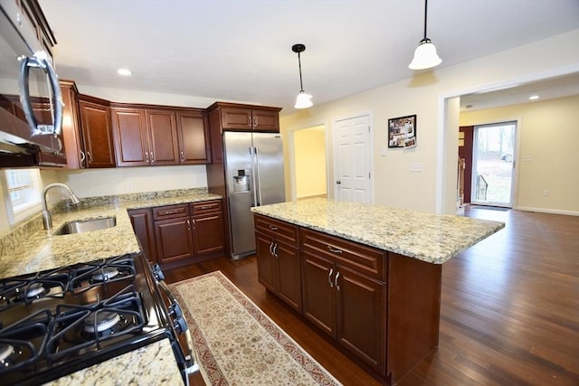 kitchen featuring light stone countertops, a center island, sink, stainless steel appliances, and pendant lighting