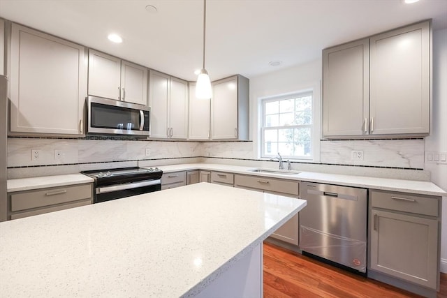 kitchen featuring light stone countertops, sink, stainless steel appliances, backsplash, and decorative light fixtures