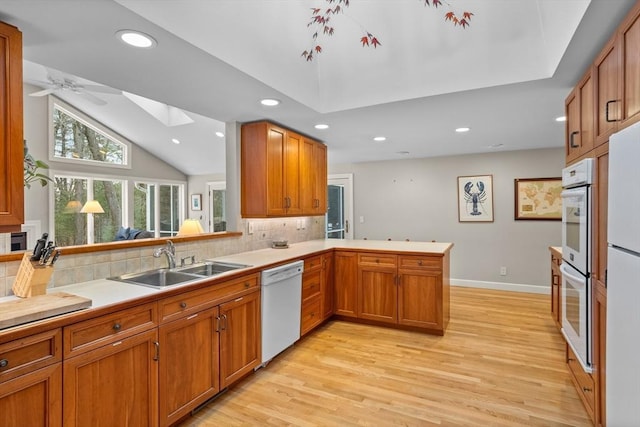 kitchen featuring sink, kitchen peninsula, white appliances, vaulted ceiling with skylight, and decorative backsplash