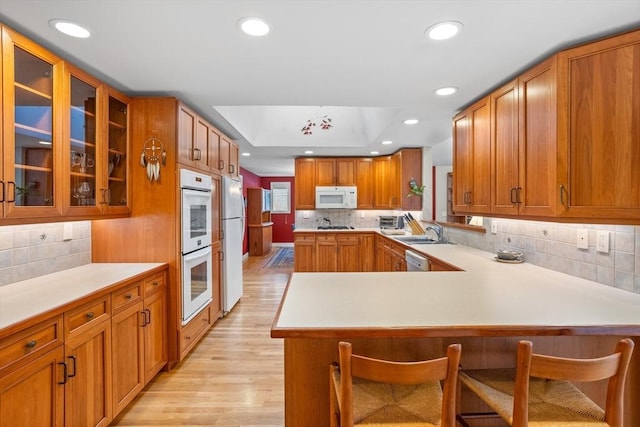 kitchen featuring kitchen peninsula, a kitchen breakfast bar, white appliances, a tray ceiling, and light wood-type flooring