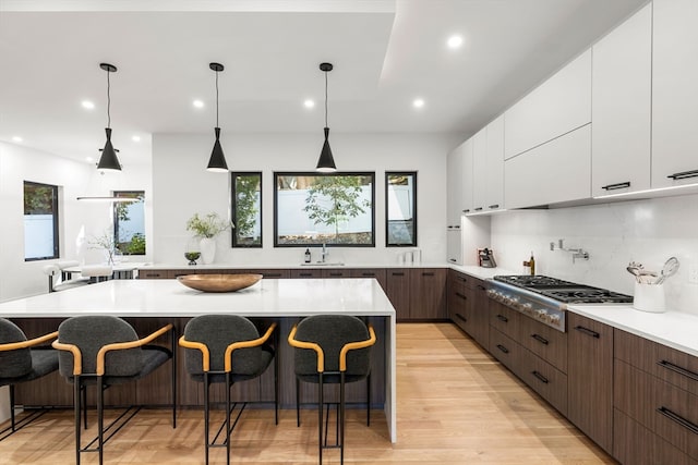 kitchen with stainless steel gas stovetop, a center island, light hardwood / wood-style floors, sink, and a kitchen bar