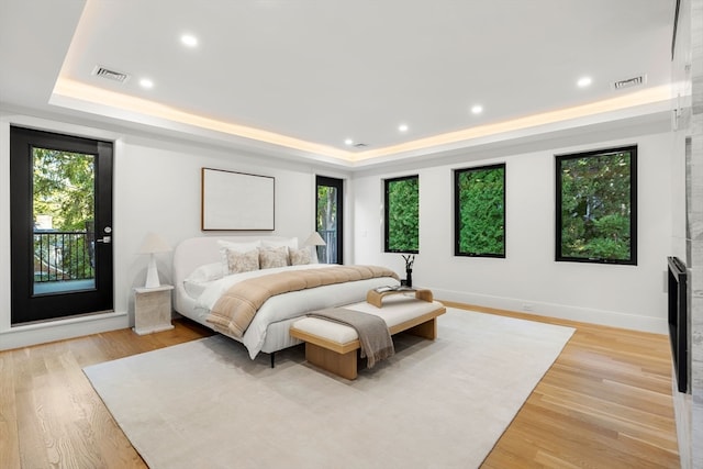 bedroom with light hardwood / wood-style flooring, access to exterior, and a tray ceiling