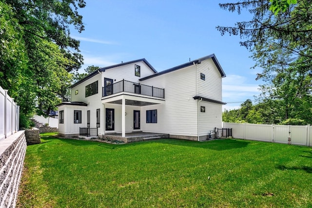 back of property with a balcony, a patio area, and a lawn