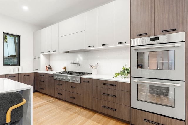 kitchen featuring stainless steel gas cooktop, tasteful backsplash, white cabinetry, light wood-type flooring, and double oven