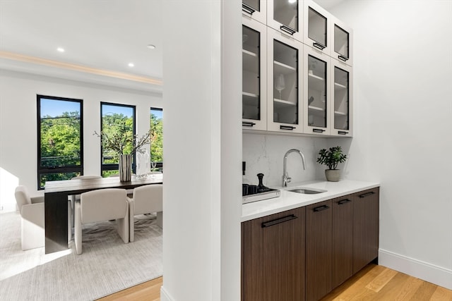 bar featuring dark brown cabinets, light hardwood / wood-style flooring, backsplash, and sink