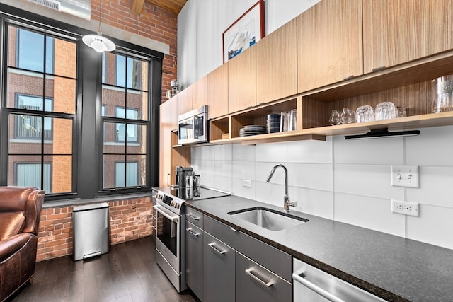 kitchen with brick wall, sink, appliances with stainless steel finishes, and dark hardwood / wood-style flooring